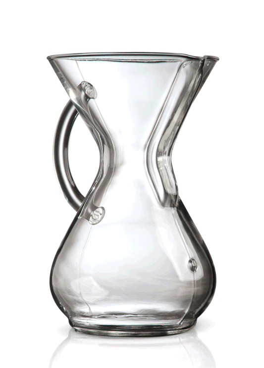 Et klart glas Chemex, Glas Kaffebrygger med håndtag, 6 Kopper (CM-6GH) med en markant timeglasform og trækrave. 6-kops-modellen er designet til pour-over-kaffebrygning, med en tud til hældning og et håndtag for let greb. Billedet er sat mod en hvid baggrund.