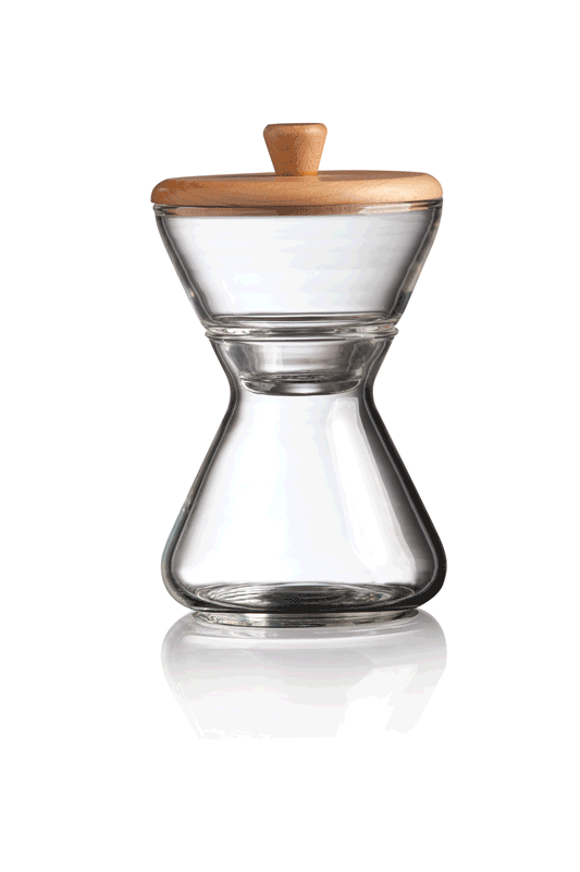 En klar timeglasformet glasbeholder, lavet af mundblæst glas med trælåg. Chemex Håndlavet Glas Sukker- og Fløde-sæt (CCS)'s brede åbning i toppen tilspidser i midten, før den udvider sig udad igen, hvilket skaber et symmetrisk, elegant design, der er perfekt til kaffeservering.