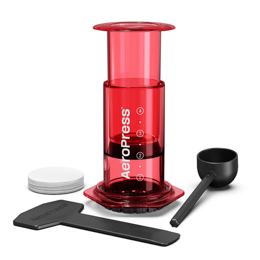 Rød AeroPress, Clear Kaffebrygger fra Aeropress, med et stempel, kammer med markeringer, scoop, omrører, filterholder lavet af Tritan™ og papirfiltre – alt sammen på en hvid baggrund.