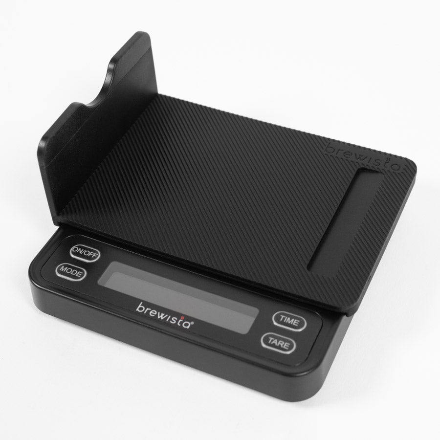 Brewista Smart Scale 3 har et sort minimalistisk design med en struktureret platform til præcisionsmålinger, et elektronisk display med power-, mode-, time- og tara-knapper. Brewista-mærkenavnet vises elegant.