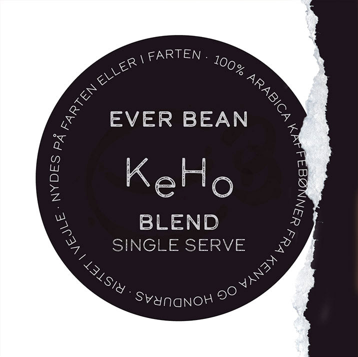 En cirkulær etiket til EverBean Single Serve KeHo-blandingen fremhæver tekst på dansk omkring 100 % Arabica-kaffebønner fra Kenya og Honduras, sat mod en mørk baggrund med en struktureret rift langs den ene kant.