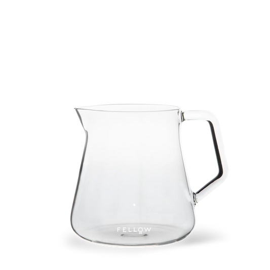 En klar, minimalistisk glaskaraffel med hank, med et elegant design, der er ideelt til at opnå det perfekte kaffe-til-vand forhold. Basen på Fellow, Mighty Small Glas Karaffel har mærket "Fellow" trykt i hvidt. Karaflen er tom og sat mod en almindelig hvid baggrund.