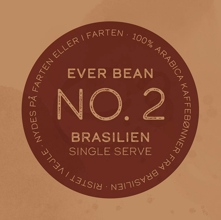 En cirkulær etiket med brun baggrund til EverBeans "Single Serve, No. 02 · Brasilen" viser tekst med "100% Arabica kaffebønner fra Brasilien", der fejres for deres lave syrlighed, sammen med sætninger på et andet sprog, der understreger bekvemmelighed og nydelse.